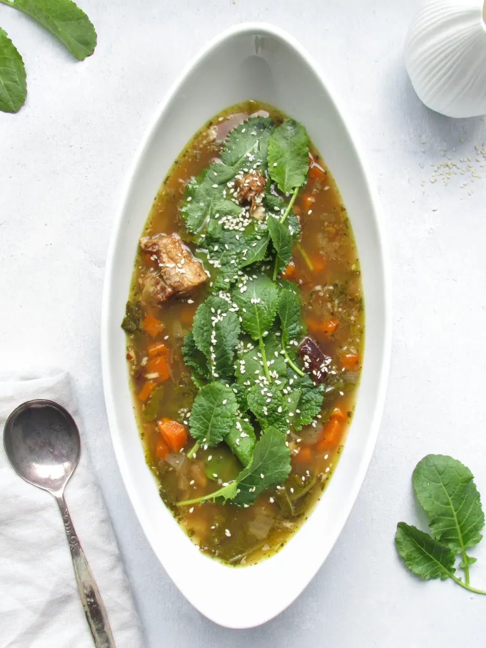 Oval bowl of pork and kale soup with sesame seeds