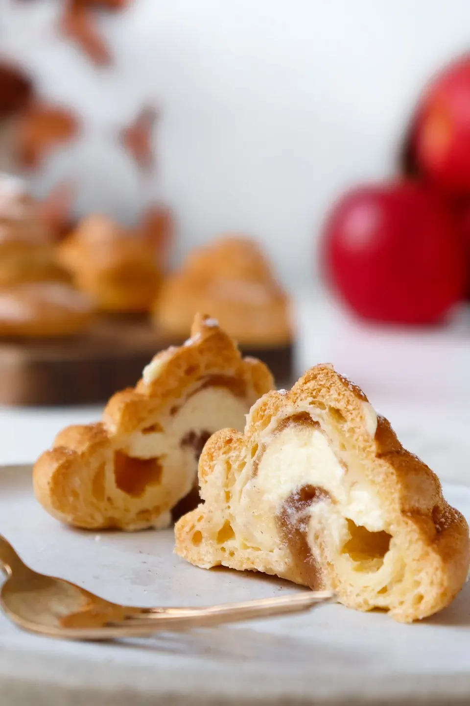 Cut apple spiced profiteroles with cream filling on white surface