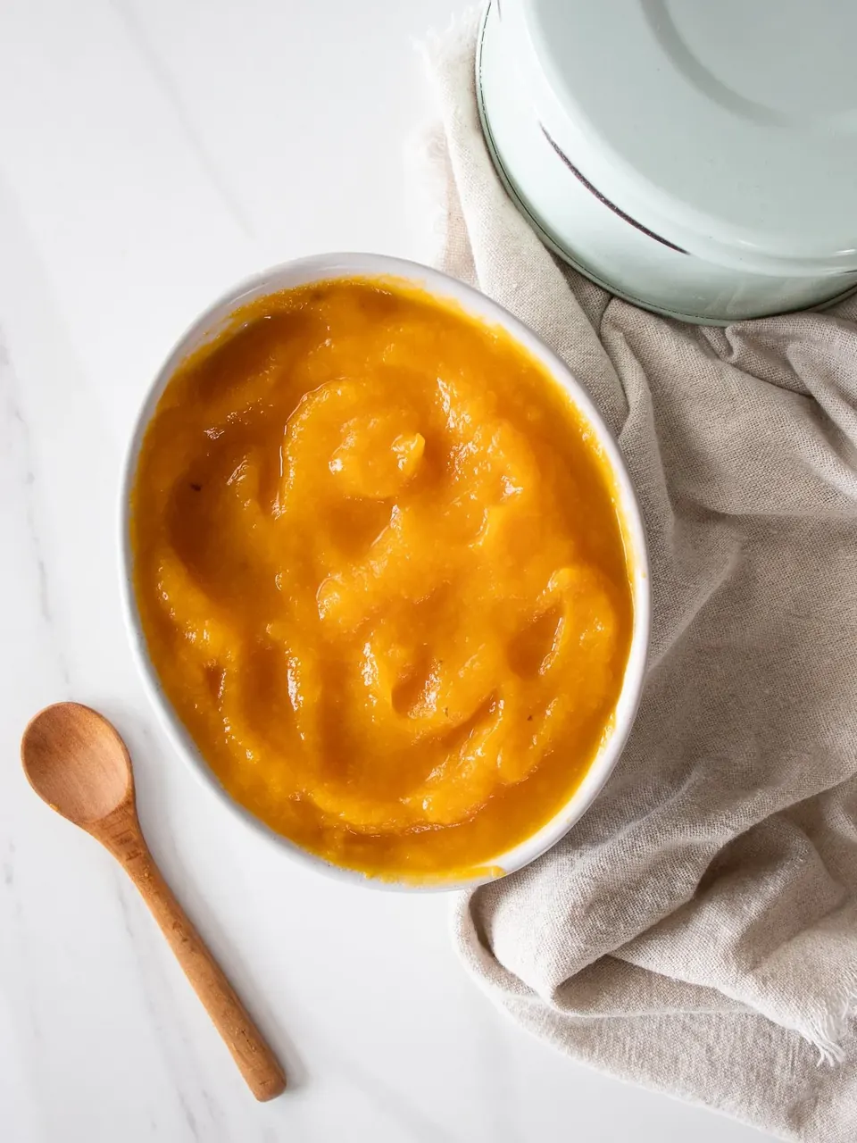 Bowl of smooth pumpkin puree with wooden spoon on counter