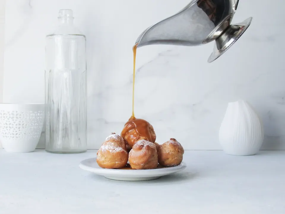 Caramel sauce poured over powdered sugar doughnut holes on plate